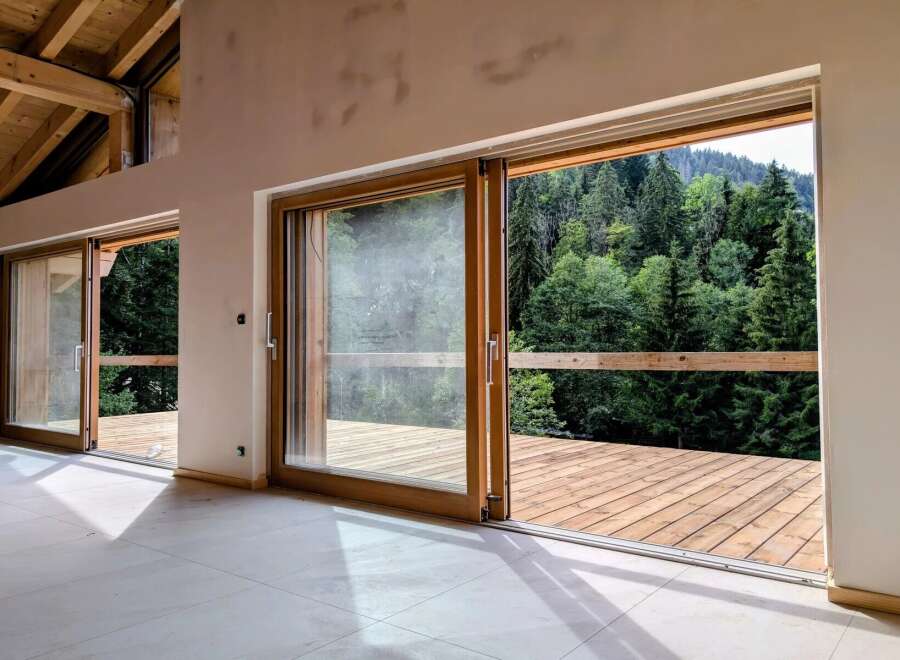 Experience seamless indoor-outdoor living with expansive sliding glass doors that open onto a spacious wooden deck, offering breathtaking views of a lush, green forest.