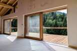Experience seamless indoor-outdoor living with expansive sliding glass doors that open onto a spacious wooden deck, offering breathtaking views of a lush, green forest.