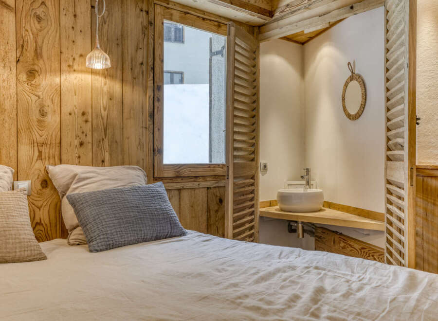 Experience rustic charm in this cozy bedroom featuring wooden paneling and a unique window design.