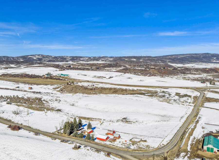 Discover this expansive rural property featuring a charming farmstead with multiple red barns and a large green agricultural building, all set against a backdrop of snow-dusted fields and rolling hills.