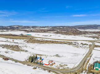 Discover this expansive rural property featuring a charming farmstead with multiple red barns and a large green agricultural building, all set against a backdrop of snow-dusted fields and rolling hills.