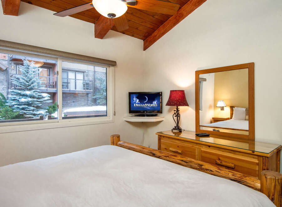 This cozy bedroom features a rustic wooden bed frame and a charming view of the snowy outdoors.