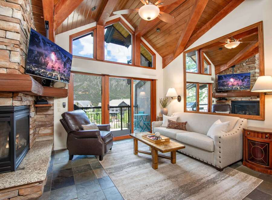 Experience luxury mountain living in this stunning living room featuring a grand stone fireplace and a vaulted wood-beamed ceiling.