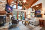 Experience luxury mountain living in this stunning living room featuring a grand stone fireplace and a vaulted wood-beamed ceiling.
