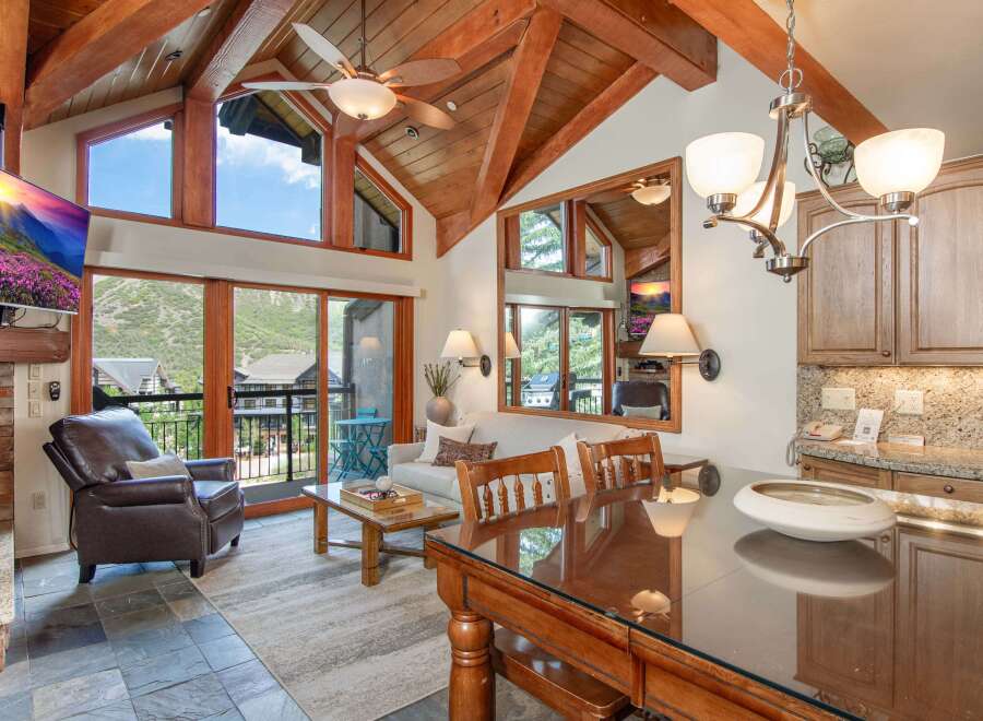 Experience luxury mountain living in this stunning condo featuring vaulted ceilings with exposed wooden beams and a wall of windows offering breathtaking views.