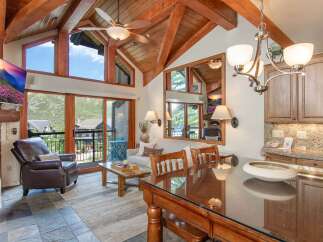 Experience luxury mountain living in this stunning condo featuring vaulted ceilings with exposed wooden beams and a wall of windows offering breathtaking views.