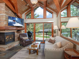 Experience mountain living in this stunning living room featuring a cozy stone fireplace and a large flat-screen TV perfect for relaxing after a day on the slopes.