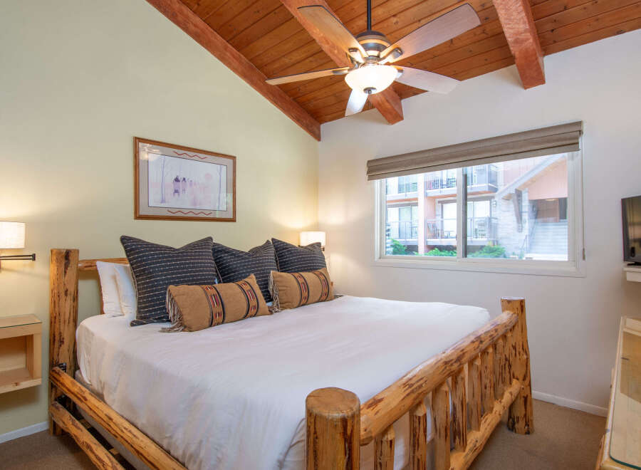 Experience rustic charm in this cozy bedroom featuring a sturdy log bed and a vaulted wood-beamed ceiling with a ceiling fan.