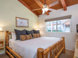 Experience rustic charm in this cozy bedroom featuring a sturdy log bed and a vaulted wood-beamed ceiling with a ceiling fan.