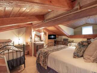 Experience rustic charm in this unique attic bedroom, featuring exposed wooden beams and a cozy, sloped ceiling.