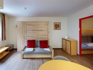 Discover this cozy apartment featuring a comfortable living area with a pull-out sofa and vibrant red cushions.