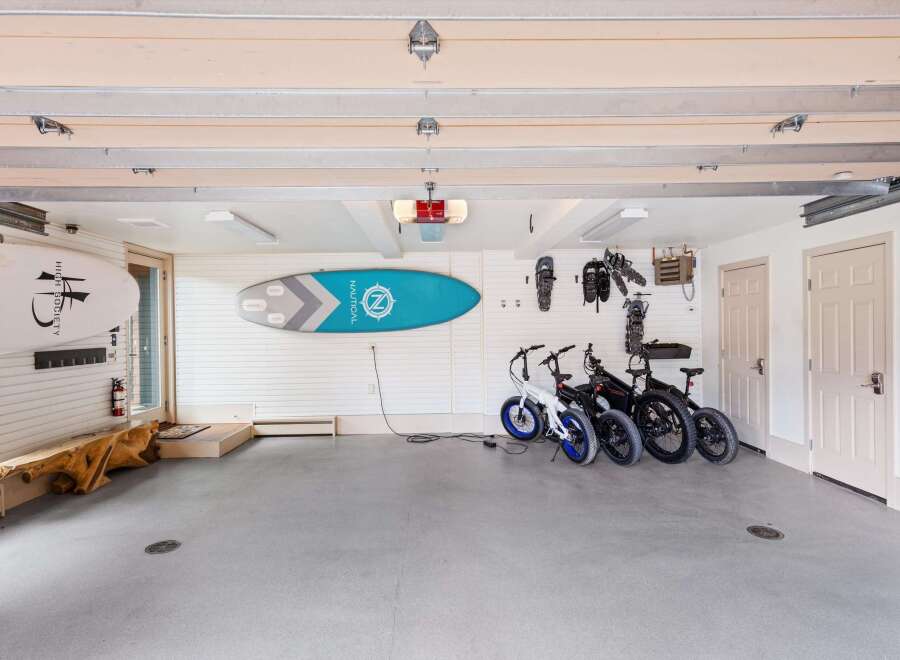 This spacious garage offers ample storage and recreational space, featuring two surfboards mounted on the wall and a row of electric bikes ready for adventure.