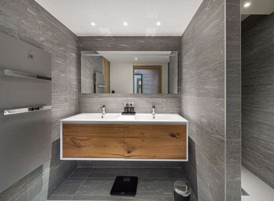 This modern bathroom boasts a sleek design with its gray tiled walls and wooden vanity.