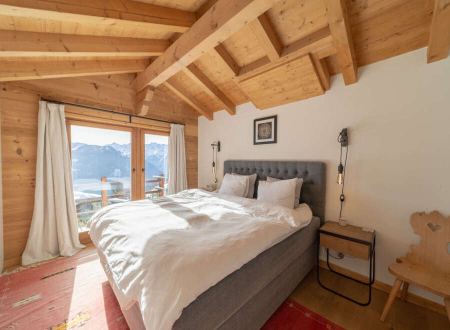 Experience the charm of this stunning bedroom with its exposed wooden beams and breathtaking mountain views.