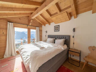 Experience the charm of this stunning bedroom with its exposed wooden beams and breathtaking mountain views.
