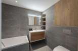 This modern bathroom features a sleek design with gray tiled walls and a wooden vanity.