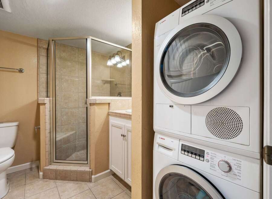 This bathroom features a modern design with a glass-enclosed shower, a sleek vanity, and a convenient stacked washer and dryer.