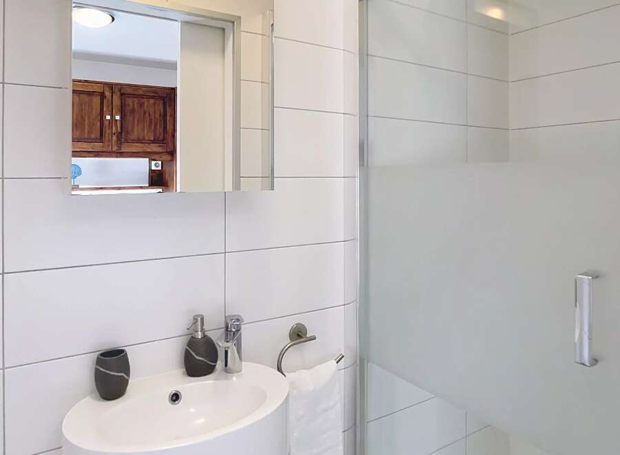 This modern bathroom features a sleek, white design with a glass shower enclosure.