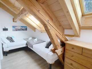 This charming bedroom features a unique architectural design with exposed wooden beams and a slanted ceiling, creating a cozy and inviting atmosphere.