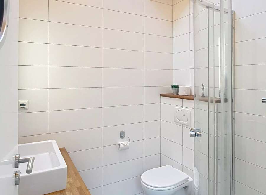 This modern bathroom features a sleek design with white tiles and a glass shower enclosure.