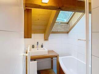 This stunning bathroom boasts a unique design with exposed wooden beams and a skylight, creating a warm and inviting atmosphere.