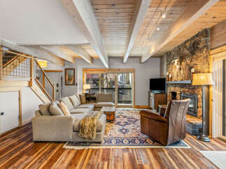 This stunning living room boasts a cozy ambiance with its stone fireplace and exposed wooden beams.