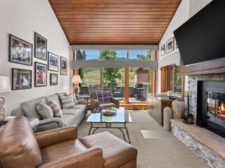 Experience luxurious living in this stunning mountain retreat, featuring a spacious living area with a cozy fireplace and a large window offering breathtaking views.