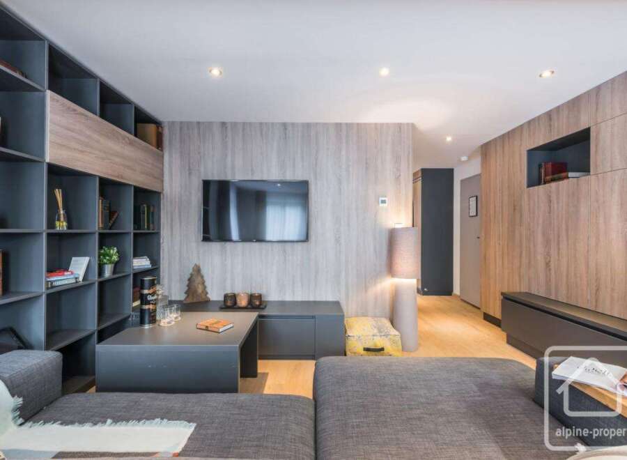 Discover modern living in this stylish property, featuring a sleek entertainment area with a mounted TV and a cozy seating arrangement.