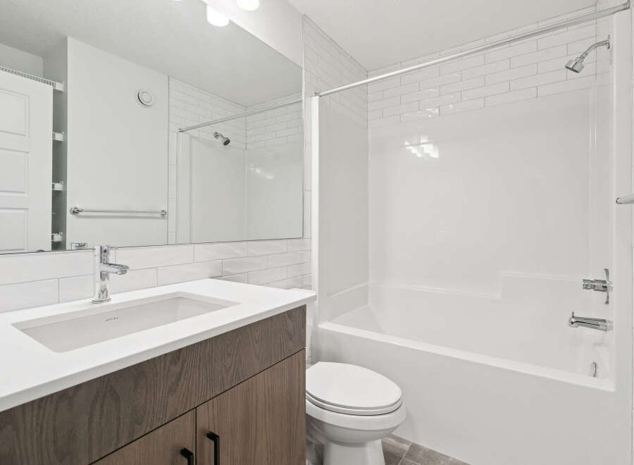 This modern bathroom features a sleek design with a white vanity and a matching white bathtub.