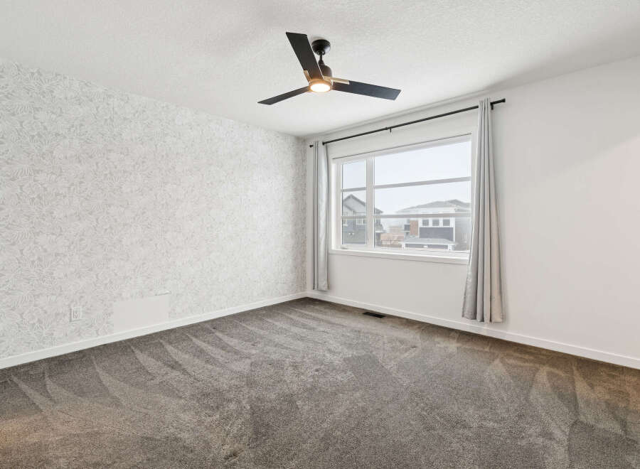 Step into this bright and airy bedroom, featuring a modern ceiling fan and a large window that floods the space with natural light.