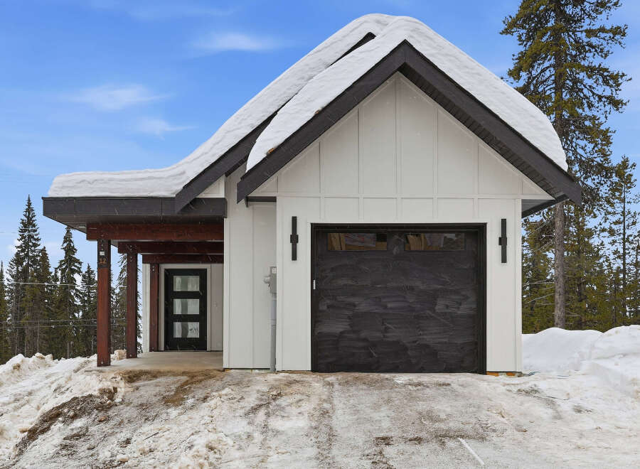 This charming property features a modern farmhouse design with a striking black garage door and a snow-covered roof, creating a cozy winter aesthetic.