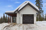 This charming property features a modern farmhouse design with a striking black garage door and a snow-covered roof, creating a cozy winter aesthetic.