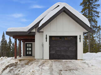 This charming property features a modern farmhouse design with a striking black garage door and a snow-covered roof, creating a cozy winter aesthetic.