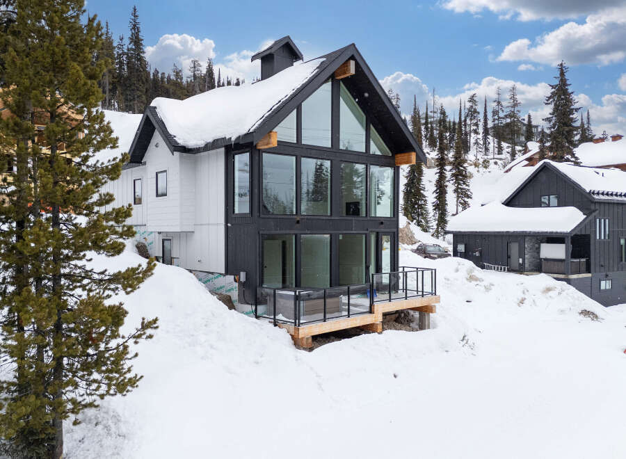 This stunning modern home boasts a striking black and white exterior, perfectly complementing its snowy mountain surroundings.