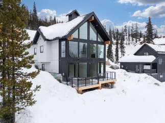 This stunning modern home boasts a striking black and white exterior, perfectly complementing its snowy mountain surroundings.