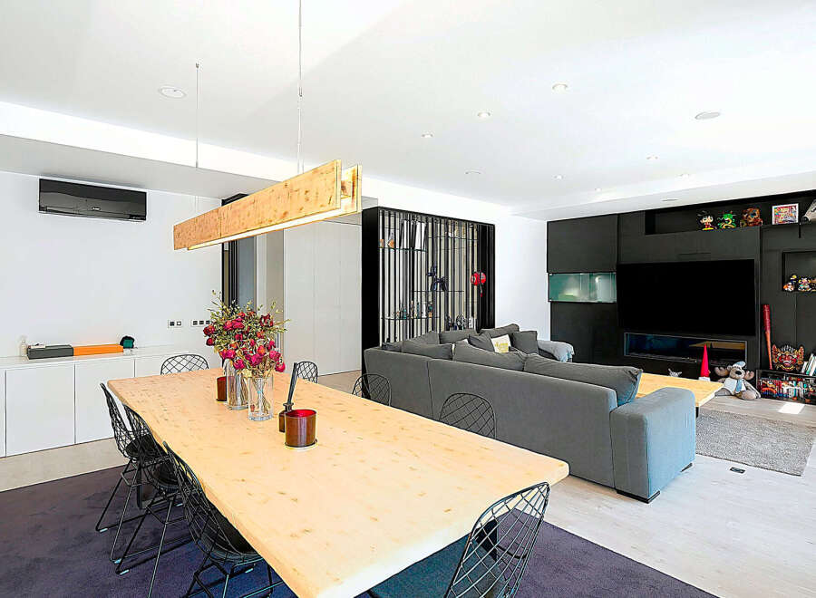 This modern living space features a stunning dining area with a large wooden table and stylish wire chairs.