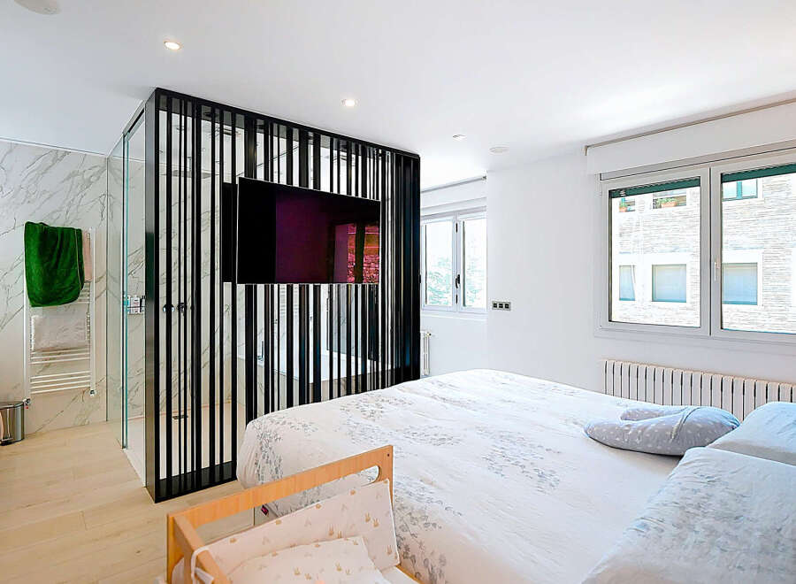 This modern bedroom boasts a sleek design with a stylish partition featuring a mounted TV, creating a unique focal point.