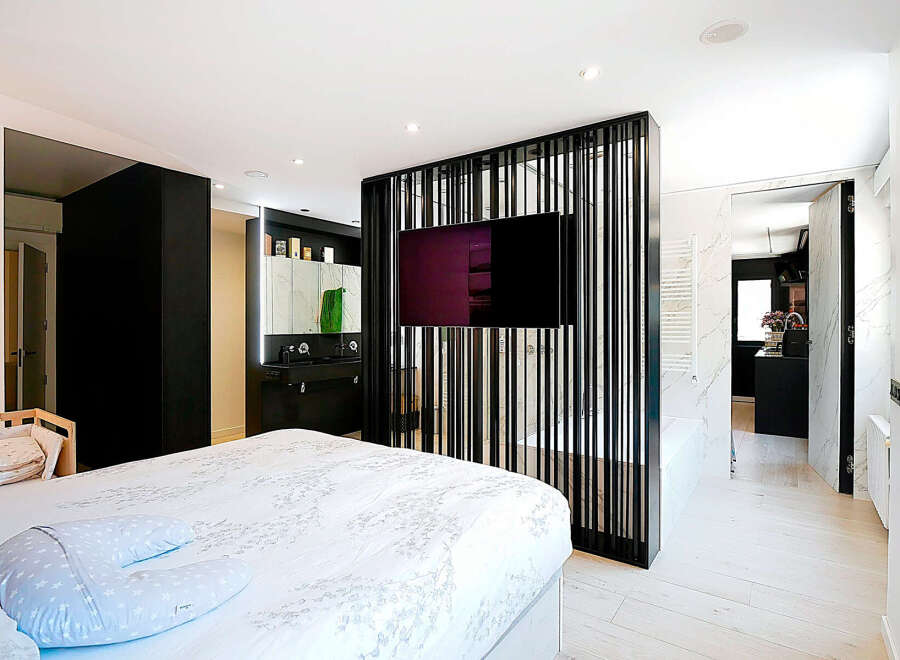 This modern bedroom boasts a sleek design with a stylish black partition featuring a mounted TV, separating the sleeping area from the bathroom.