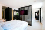 This modern bedroom boasts a sleek design with a stylish black partition featuring a mounted TV, separating the sleeping area from the bathroom.