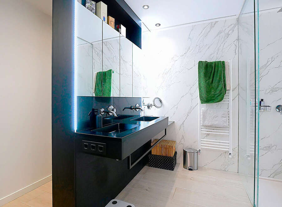 This modern bathroom boasts a sleek, minimalist design with a black double sink and elegant marble-patterned walls.