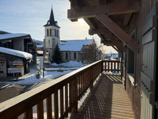 Experience the charm of a winter wonderland from this charming balcony, offering a picturesque view of a snow-covered village with a historic church.
