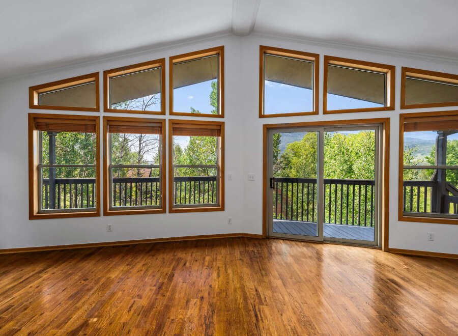 Experience breathtaking views from this stunning living room, featuring a wall of large windows and a sliding glass door that opens to a spacious deck.