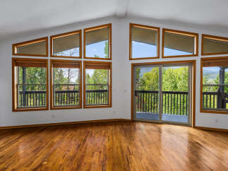 Experience breathtaking views from this stunning living room, featuring a wall of large windows and a sliding glass door that opens to a spacious deck.