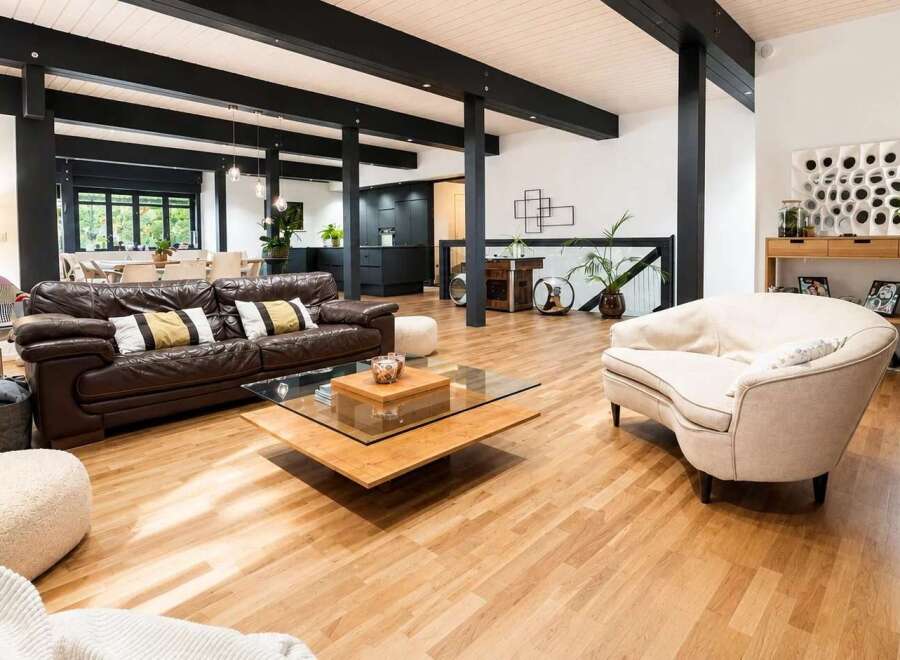 Experience modern living in this spacious open-concept home featuring a sleek dark kitchen and a comfortable living area with a rich leather sofa.