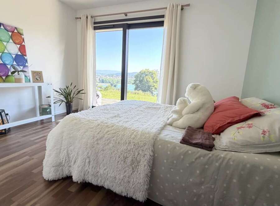 Experience breathtaking views from this serene bedroom, featuring a plush white comforter and a large window overlooking a picturesque landscape.