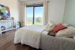 Experience breathtaking views from this serene bedroom, featuring a plush white comforter and a large window overlooking a picturesque landscape.