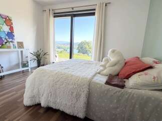 Experience breathtaking views from this serene bedroom, featuring a plush white comforter and a large window overlooking a picturesque landscape.