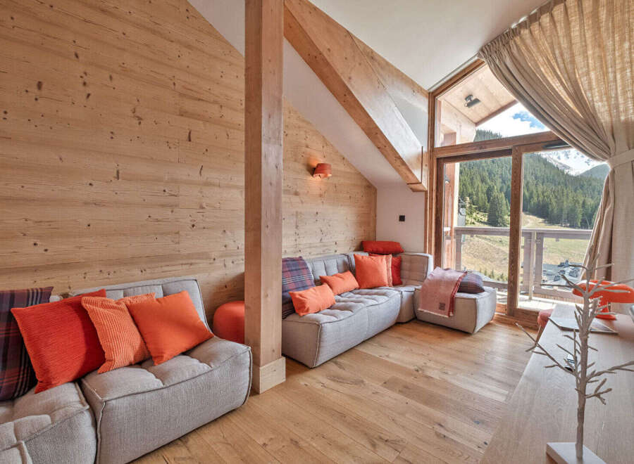 Experience luxurious mountain living in this stunning chalet-style living room, featuring warm wood paneling and a cozy sectional sofa adorned with vibrant orange and plaid cushions.