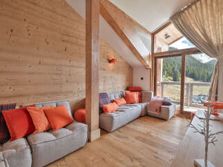 Experience luxurious mountain living in this stunning chalet-style living room, featuring warm wood paneling and a cozy sectional sofa adorned with vibrant orange and plaid cushions.