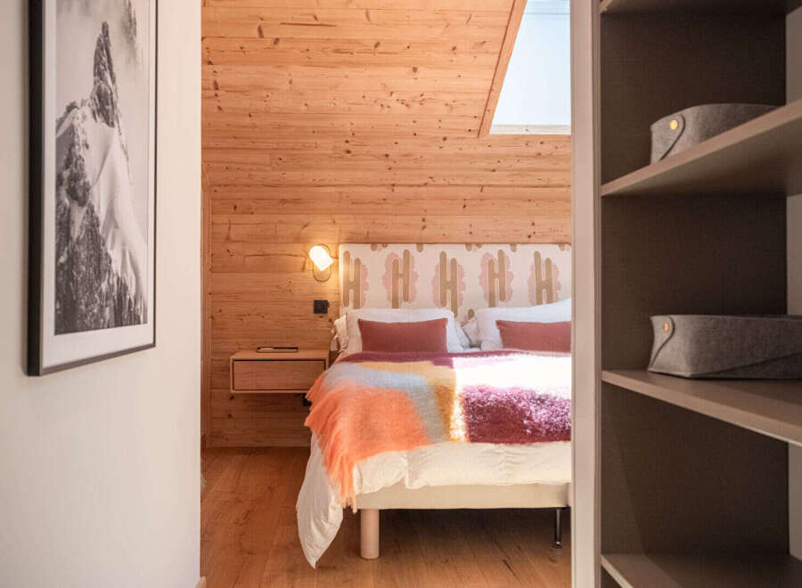 Experience cozy mountain living in this charming bedroom featuring warm wood paneling and a comfortable bed adorned with a vibrant, textured throw.